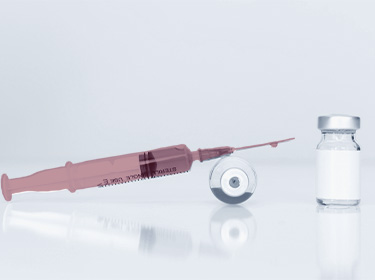 a pharmaceutical vial lies on its side on the floor and a red filled glass syringe lies on top of it